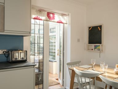 A kitchen with a toaster on the counter a wooden dining table with chairs and glass doors leading to a sunroom at Rockpool in Harlyn Bay near St Merryn