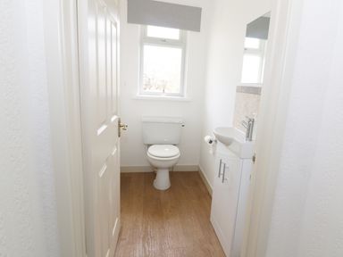 A small bathroom with a toilet a sink with cabinet a mirror and a window at The Elms in Milford Haven
