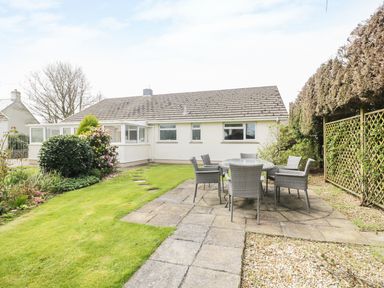 A backyard with a patio table and chairs a lawn and bushes at The Elms in Milford Haven