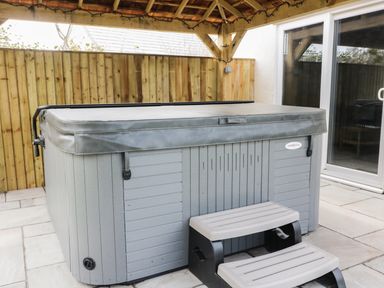 A covered hot tub with plastic steps on a tiled patio under a wooden pergola at The Elms in Milford Haven