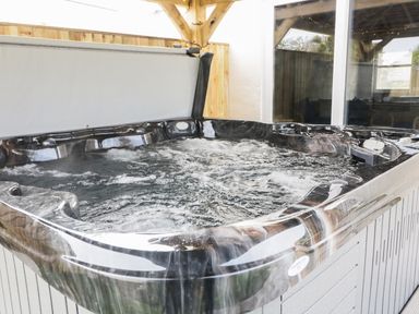 An outdoor hot tub with bubbling water under a wooden pergola next to a glass door at The Elms in Milford Haven
