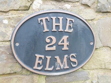 An oval house sign with the text The 24 Elms mounted on a stone wall at The Elms in Milford Haven
