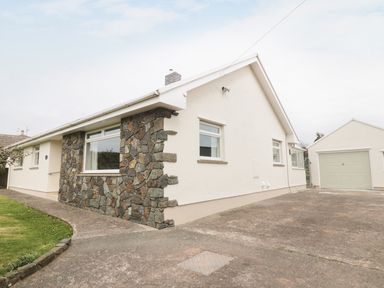 A single-story house with stone and white exterior walls and a driveway with a detached garage at The Elms in Milford Haven