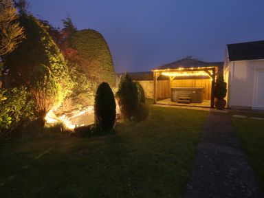 A garden with a wooden gazebo and lights beside shrubbery and a pathway at The Elms in Milford Haven