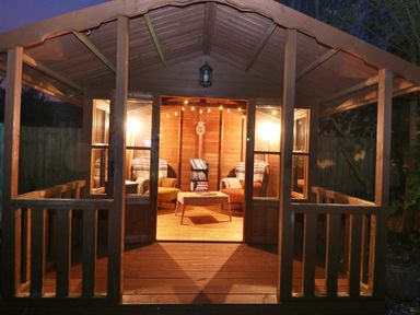 A wooden garden cabin with two armchairs a small table a bookshelf and string lights at The Elms in Milford Haven