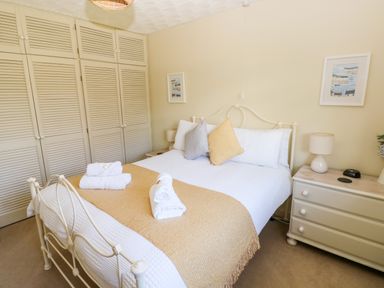 A bedroom with a metal bed frame white bedding yellow blanket and pillows built in wardrobe and bedside table with lamp at The Elms in Milford Haven