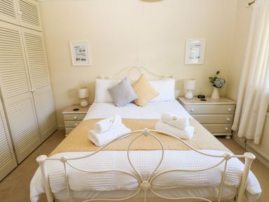 A bedroom with a double bed with two pillows and folded towels bedside tables with lamps and a vase with flowers at The Elms in Milford Haven