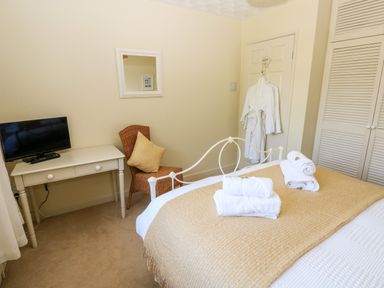 A bedroom with a bed covered in towels a white desk with a television a wicker chair and a bathrobe hanging on a door at The Elms in Milford Haven