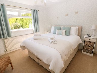 A bedroom with a double bed with pillows and towels bedside tables with lamps and window with curtains at The Elms in Milford Haven