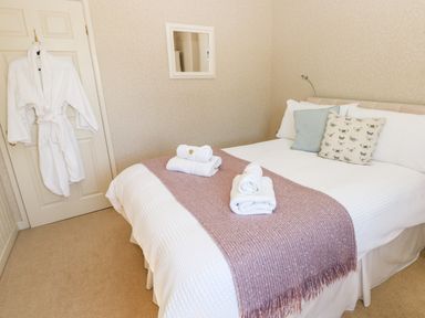 A bedroom with a double bed with white bedding and a pink runner towels on bed bathrobe hanging on door at The Elms in Milford Haven