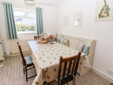 A dining area with a table covered in a patterned tablecloth surrounded by wooden chairs and a bench with cushions at The Elms in Milford Haven