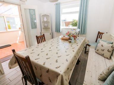 A dining room with a table covered by a patterned cloth surrounded by wooden chairs and a bench at The Elms in Milford Haven