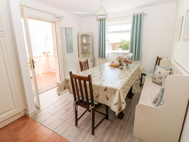 A dining room with wooden chairs a bench table with a tablecloth and flowers by a window at The Elms in Milford Haven