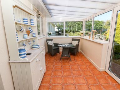 A conservatory with wicker chairs a round table a white cabinet with striped pottery and terracotta floor tiles at The Elms in Milford Haven