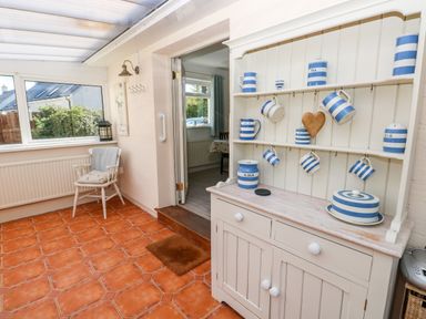 A room with terracotta tiled floor a white chair with cushion a white cupboard with blue striped pottery and an open door at The Elms in Milford Haven