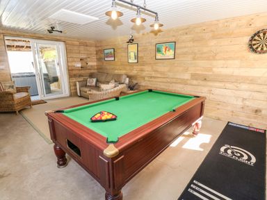 A game room with a pool table sofa armchairs and a dartboard at The Elms in Milford Haven