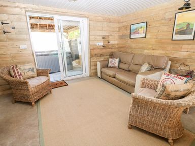 A room with wicker chairs, a sofa, throw pillows, framed pictures on wooden walls, and a sliding glass door at The Elms in Milford Haven