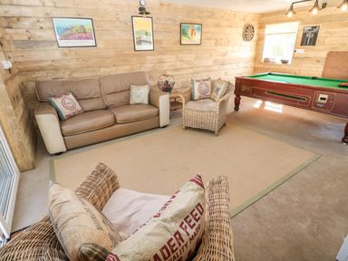 A room with a sofa, two wicker armchairs, a pool table, a dartboard, and framed pictures on wooden walls at The Elms in Milford Haven
