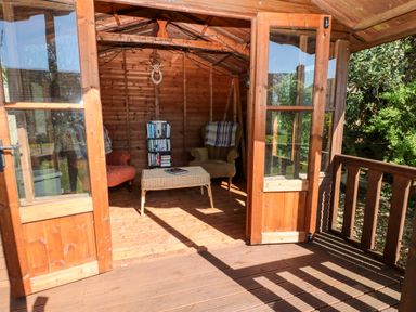 A wooden garden room with two armchairs a wicker table and a bookshelf at The Elms in Milford Haven
