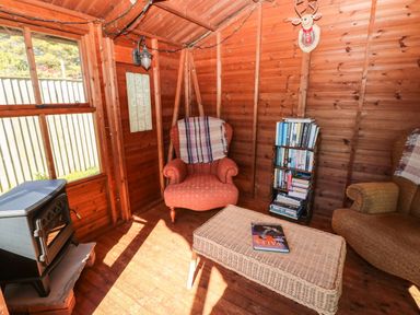 A wooden room with an armchair a wicker table a bookshelf and a stove at The Elms in Milford Haven