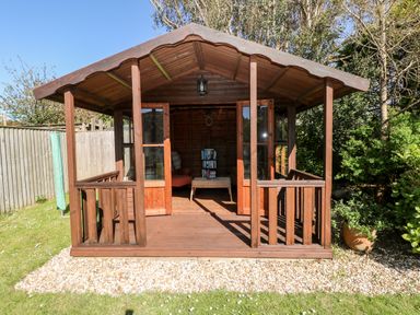 A wooden garden shed with double doors open revealing a table and books inside surrounded by grass and trees at The Elms in Milford Haven