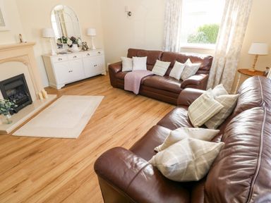 A living room with brown leather sofas cushions a white cabinet with lamps and a mirror and a fireplace at The Elms in Milford Haven