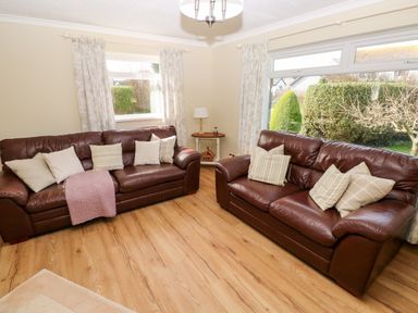 A living room with two brown leather sofas and cushions by windows with curtains at The Elms in Milford Haven