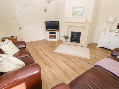 A living room with brown leather sofas a wooden floor a fireplace a television on a stand a white cabinet and a small table at The Elms in Milford Haven