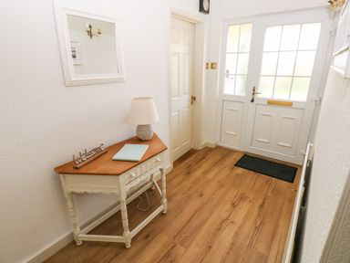 An entryway with a wooden floor a white door a small table with a lamp and a welcome sign and a wall mirror at The Elms in Milford Haven