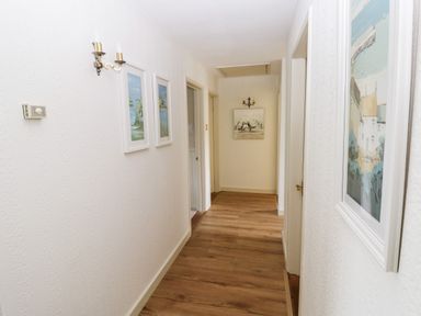 A hallway with wooden floor and white walls with framed pictures and wall lights at The Elms in Milford Haven