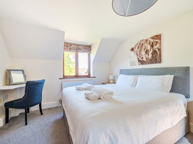A bedroom with a large bed with towels and pillows a window with a blind a blue chair and a wall picture at The Linhay in Washford near Watchet