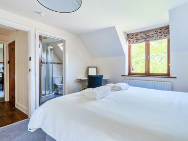 A bedroom with a bed and towels a desk and chair a window and an en suite bathroom at The Linhay in Washford near Watchet