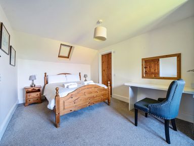 A bedroom with a wooden bed and side table a desk with a mirror and upholstered chair at The Linhay in Washford near Watchet