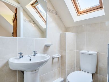 A bathroom with a sink, toilet, mirror, and skylight window at The Linhay in Washford near Watchet
