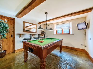 A game room with a pool table below ceiling lights and high chairs along a wall at The Linhay in Washford near Watchet