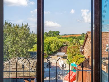 A view through a window overlooking a garden with a large chess set a slide a ping pong table and trees at The Linhay in Washford near Watchet