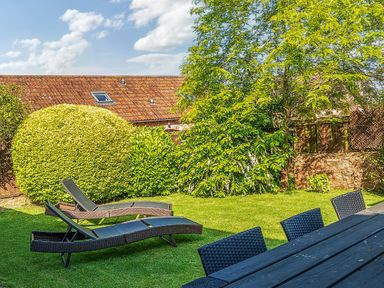 Outdoor garden with sun loungers and dining table with chairs at The Linhay in Washford near Watchet