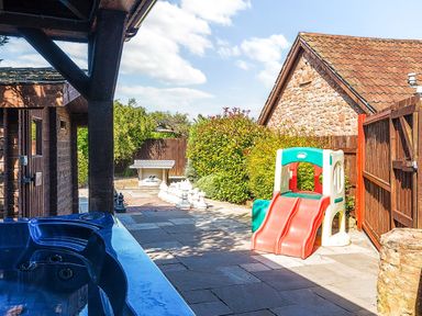 An outdoor patio area with a hot tub a large chess set a ping pong table and a children's slide at The Linhay in Washford near Watchet