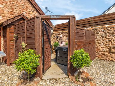 An outdoor area with wooden fencing and gate labeled The Retreat with green plants and stone walls at The Linhay in Washford near Watchet