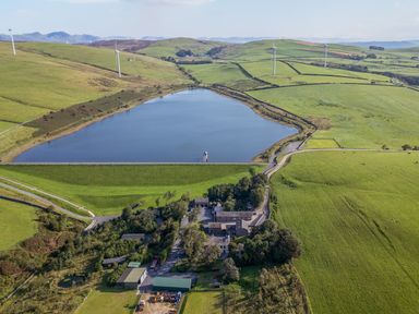 An aerial view of a lake surrounded by fields and wind turbines at Elm Lodge in Ulverston