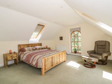 A bedroom with a wooden bed and nightstands a chair with footrest and windows at Squirrels Drey in Little Dunham near Litcham