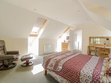 A bedroom with a bed a recliner chair a wooden dressing table and two windows in the ceiling at Squirrels Drey in Little Dunham near Litcham