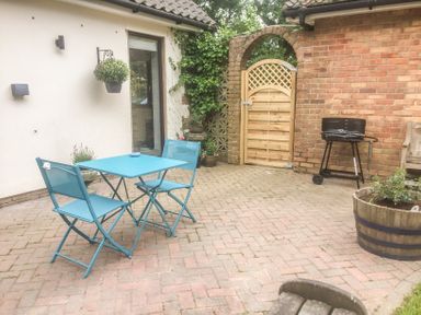 A patio with a blue table and two chairs a barbecue grill and a wooden gate at Squirrels Drey in Little Dunham near Litcham