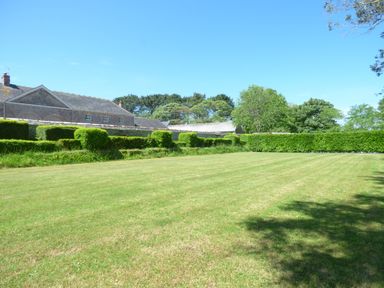 A large lawn with trimmed hedges and trees near a stone building at Parlour Cottage in Marazion