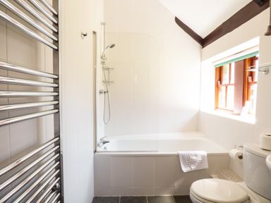 A bathroom with a bathtub shower combination a towel rail a toilet and a window at Parlour Cottage in Marazion
