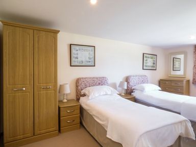 A bedroom with two single beds bedside tables lamps a wardrobe and a chest of drawers at Parlour Cottage in Marazion