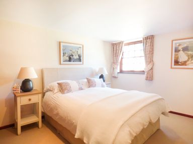 A bedroom with a bed white linens bedside tables lamps and framed pictures on walls at Parlour Cottage in Marazion