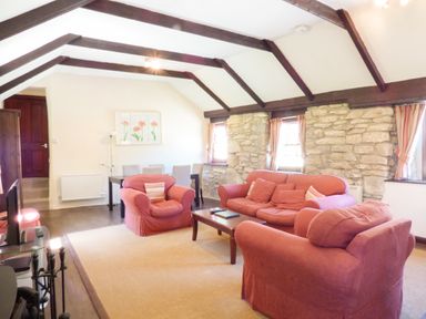 A living room with red sofas a wooden coffee table stone walls and exposed ceiling beams at Parlour Cottage in Marazion