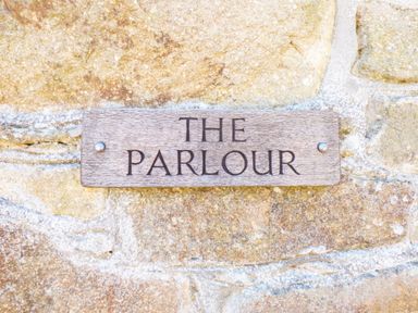 A wooden sign with the words THE PARLOUR on a stone wall at Parlour Cottage in Marazion