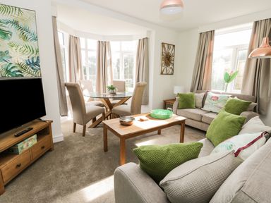 A living room with beige couches and green cushions a wooden coffee table a glass dining table with beige chairs and a television at Manor Heath Apartment 1 in Scarborough